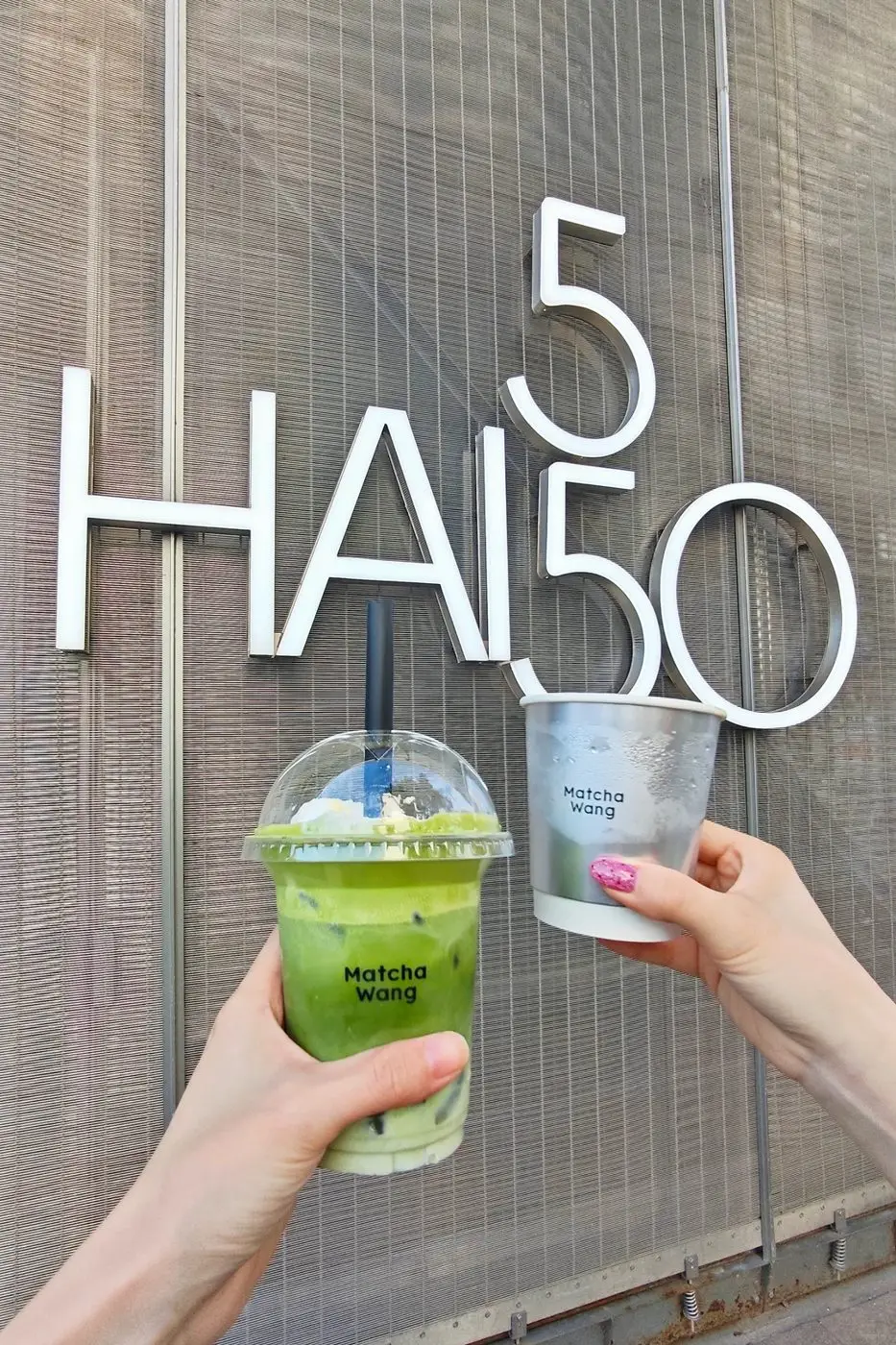 Matcha drinks held up in front of the HAI550 sign on Huaihai Middle Road